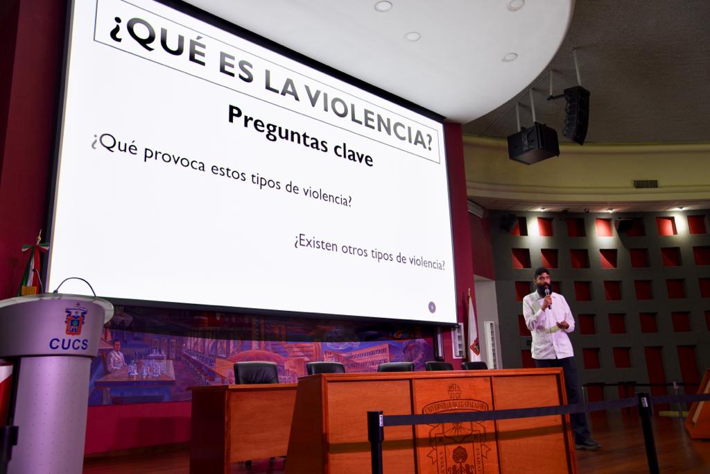 Ponente dictando conferencia, al fondo una diapositiva con el título "¿Qué es la violencia"?