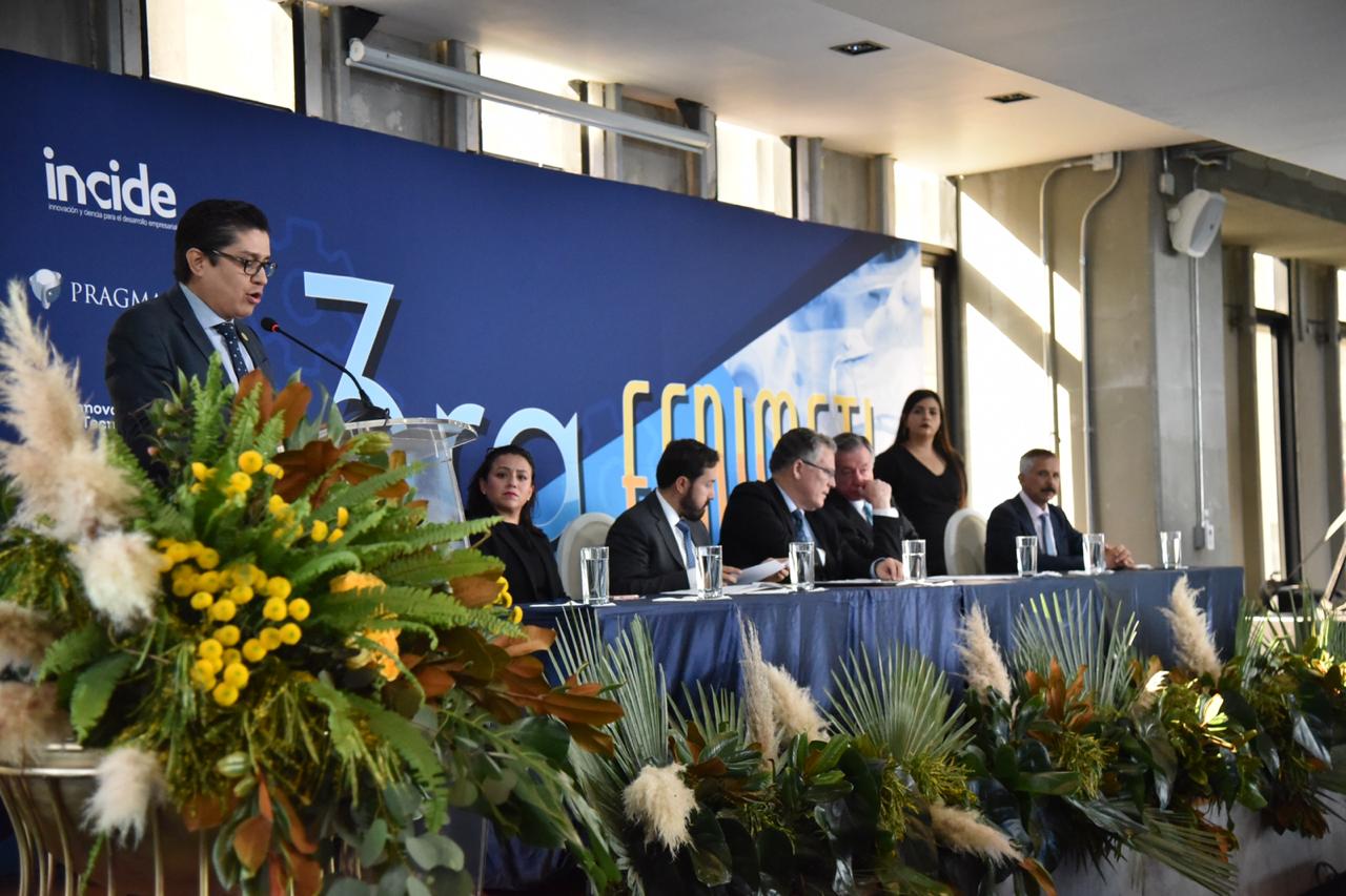 Rector CUCS en pódium haciendo uso de la palabra, al fondo los miembros del presídium