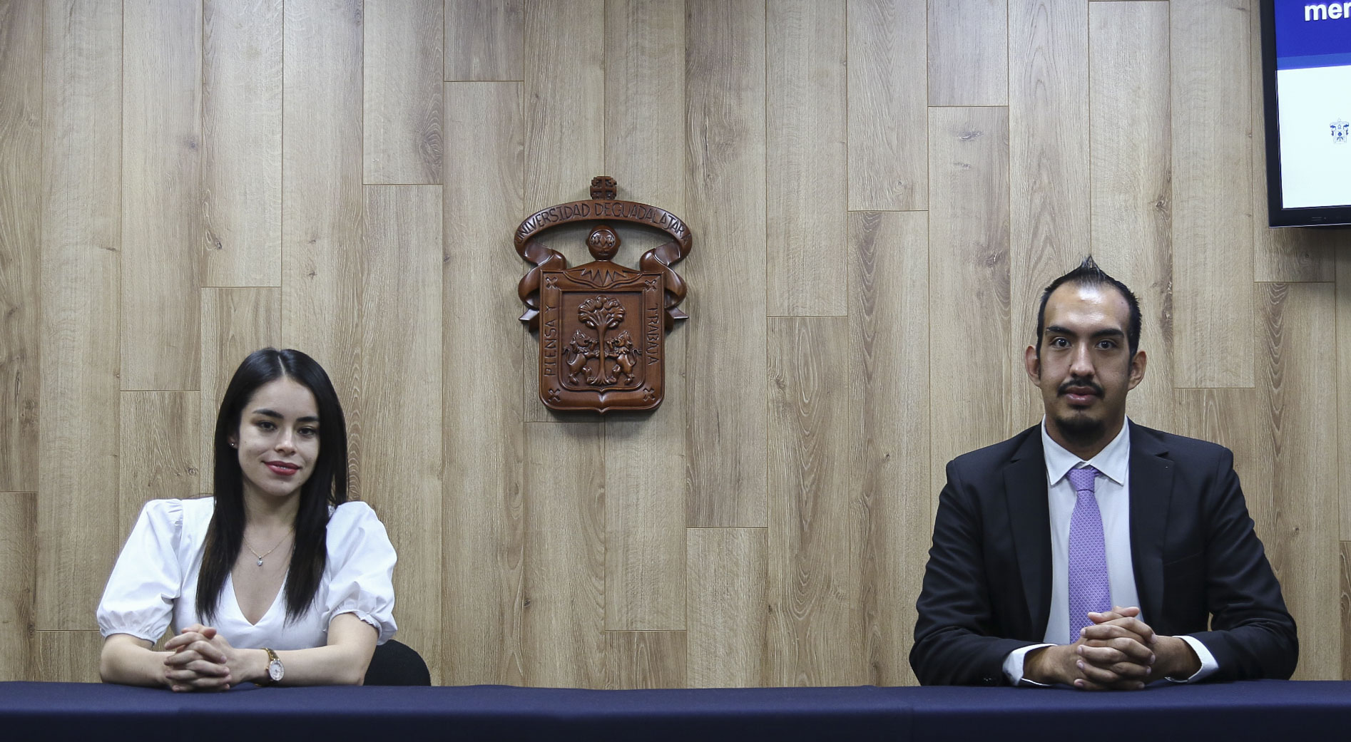 Foto de los dos premiados de CUCS, al fondo el escudo de la UdeG