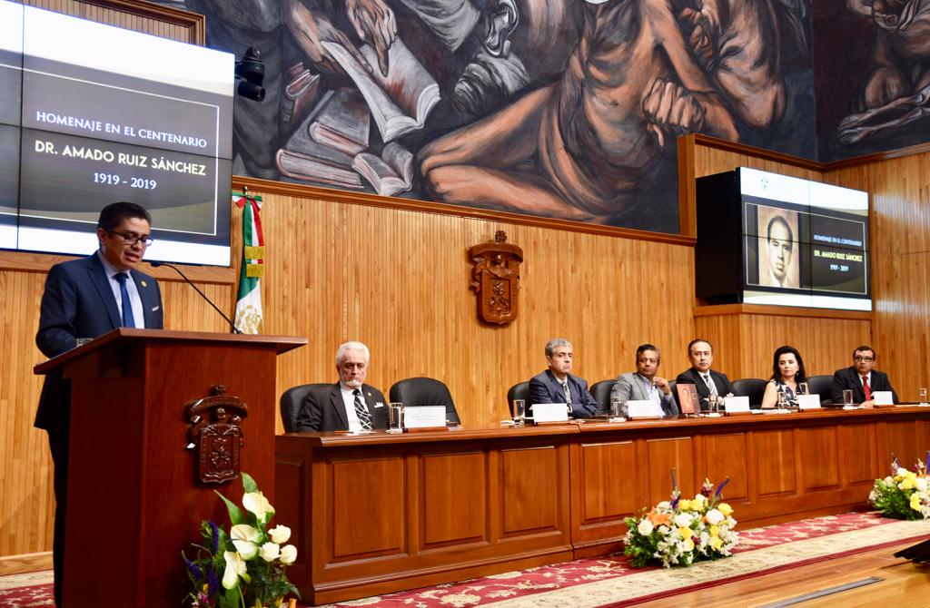 Rector CUCS al micrófono en pódium, al fondo los miembros del presídium