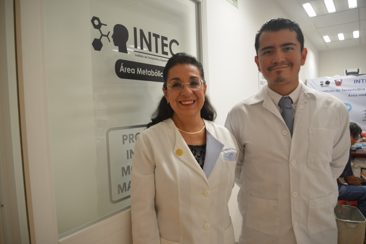 Dra. Esperanza Martínez y Dr. Luis Gaytán, atrás el letrero de INTEC en la puerta