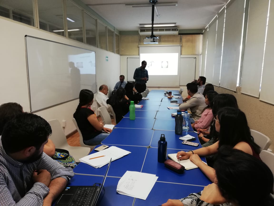 Foto general del grupo de asistentes, al fondo uno de los ponentes