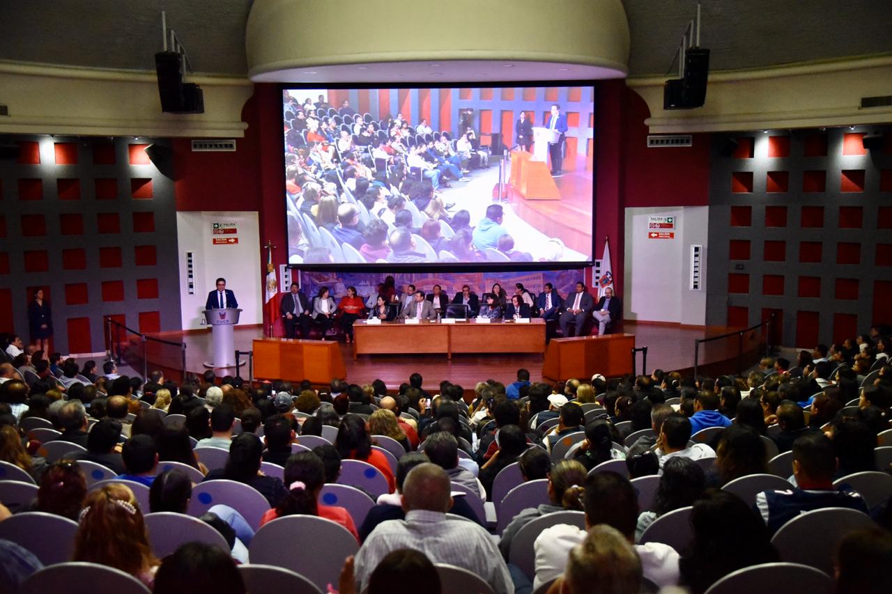 Toma general del auditorio, al fondo el rector dando mensaje en el pódium