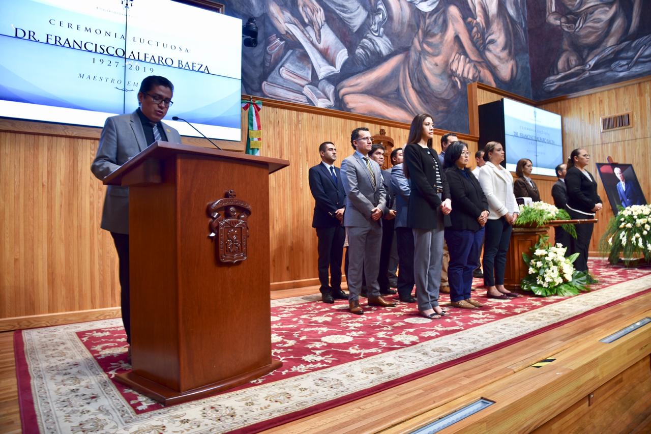 Rector del CUCS al micrófono, al fondo la guardia de honor de funcionarios y directivos del CUCS