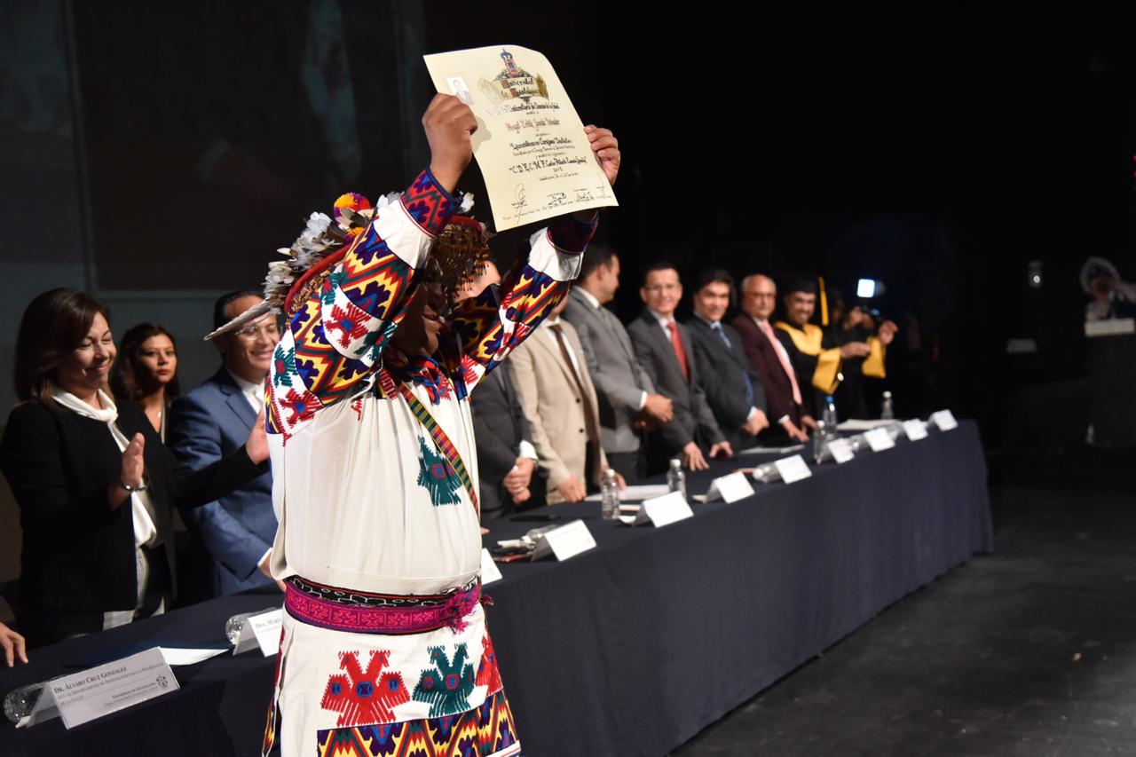 Egresado Wixárica levantando su reconocimiento en el escenario del teatro