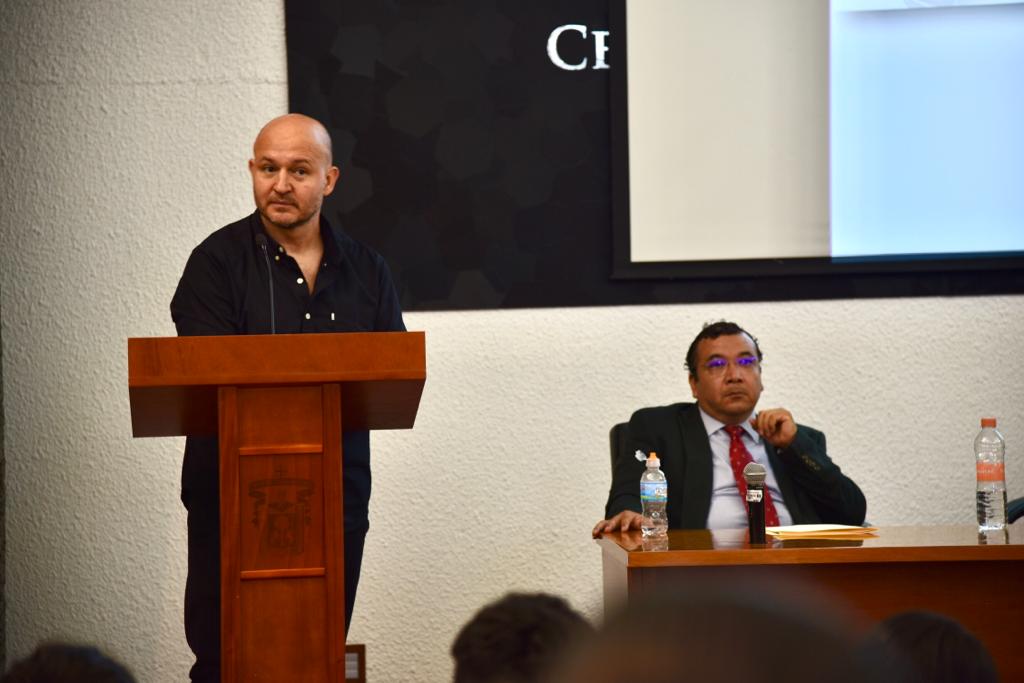 Ponente impartiendo conferencia, al fondo del coordinador de la carrera de TSU en Terapia Respiratoria