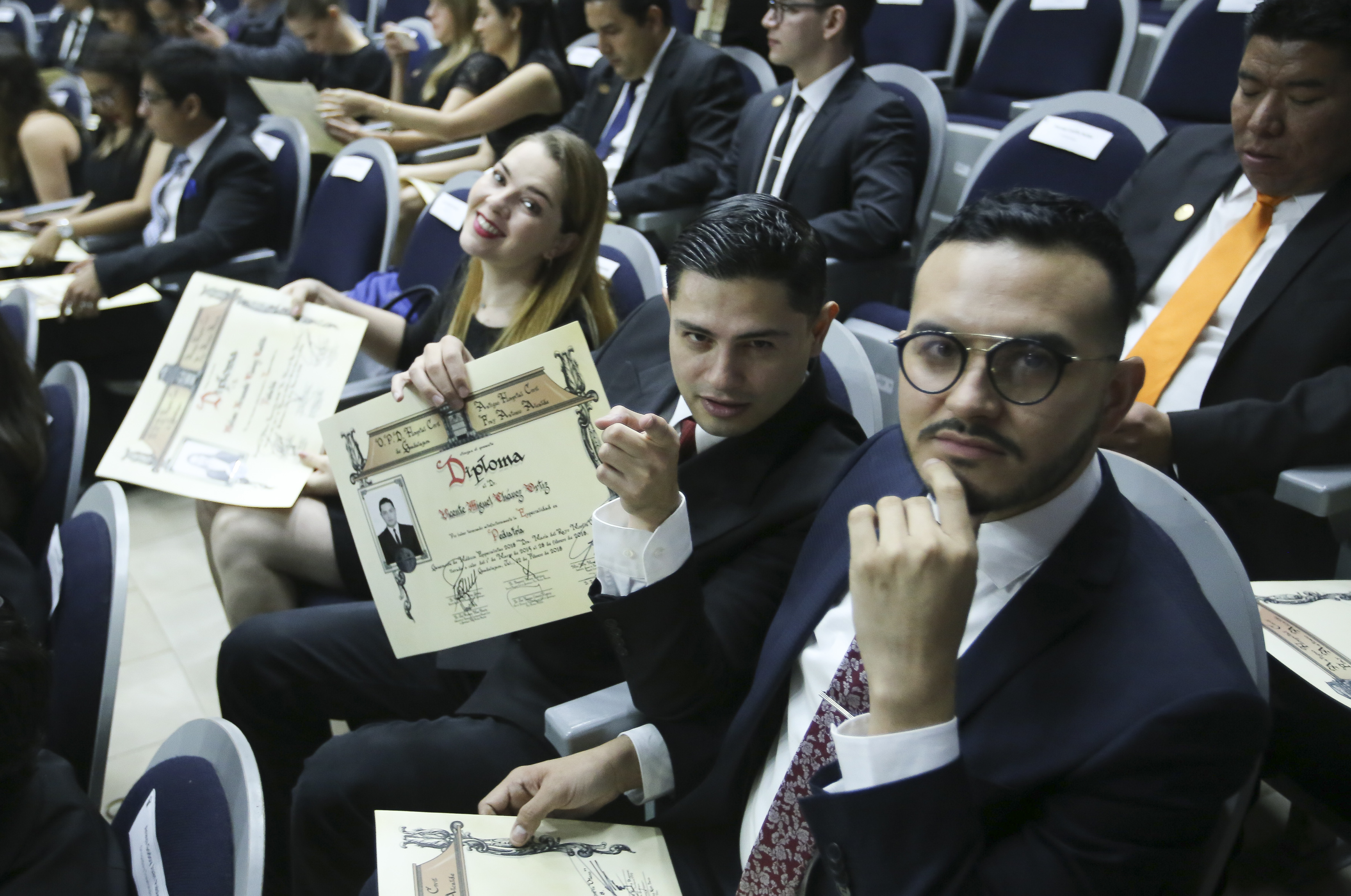Alumnos exhibiendo el diploma recibido desde sus butacas