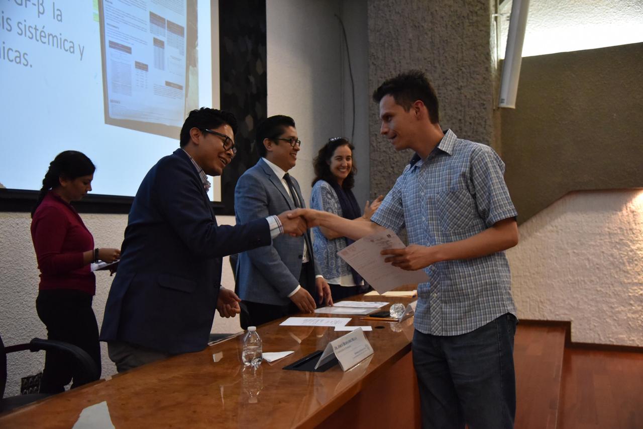Alumno ganador saludando de mano al rector quien le entrega reconocimiento