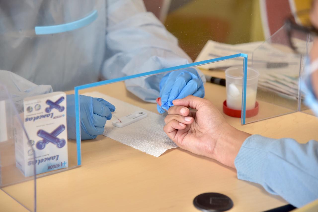 Manos del tomador de muestras con guantes pincando dedo de paciente para tomar la muestra