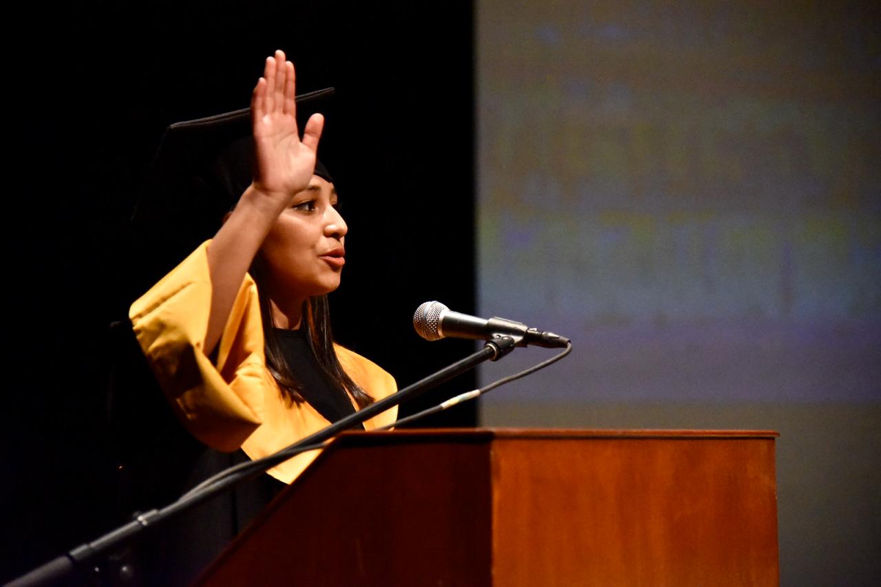 Alumna dirigiendo desde el podium el juramento hipocrático con la mano levantada