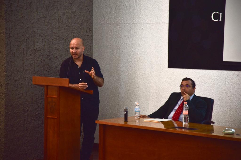 Ponente impartiendo conferencia, una diapositiva se ve en la pantalla