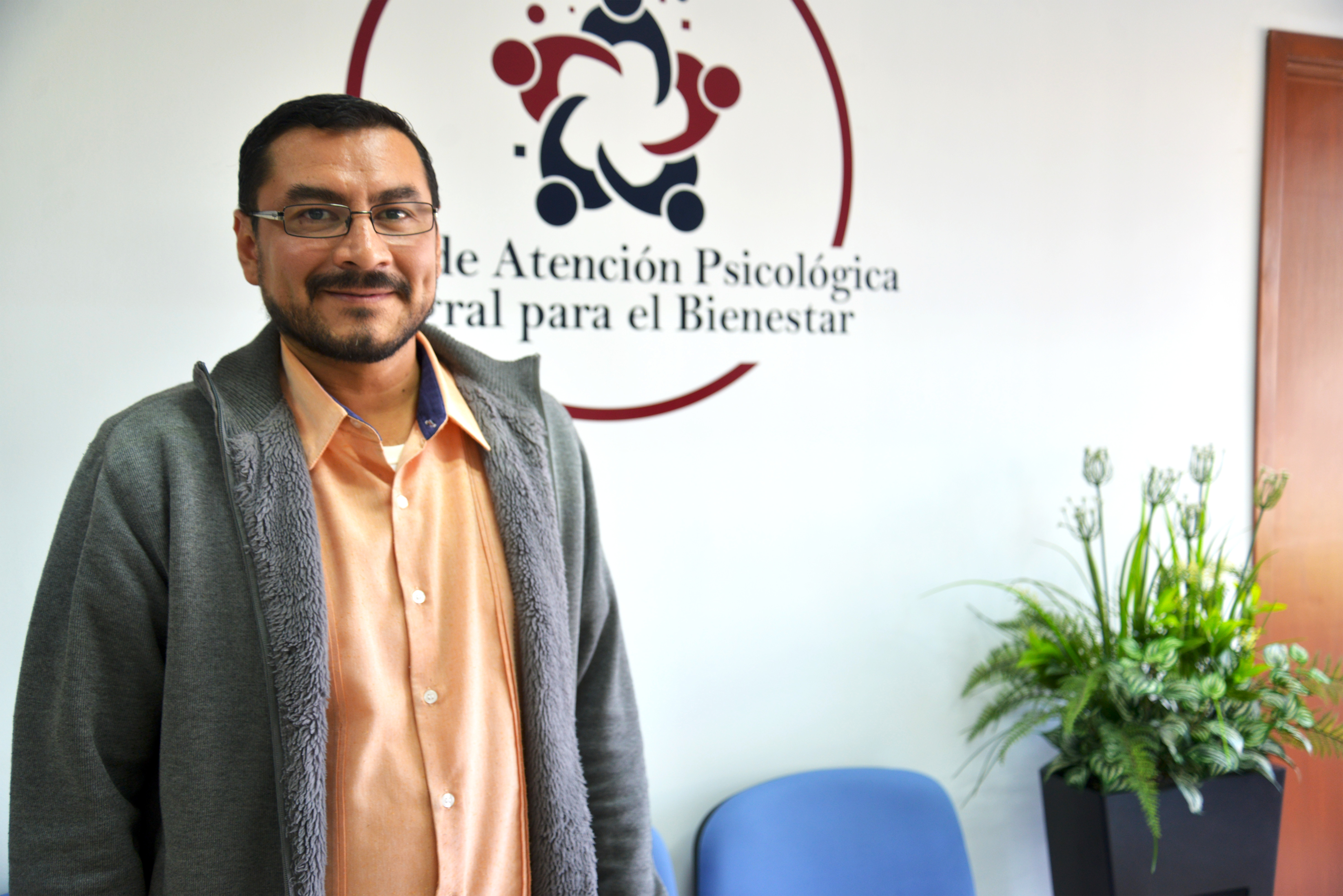 Dr. Rubén Bravo posando para la foto. Atrás logotipo de la Clínica de Atención Psicológica Integral para el Bienestar 