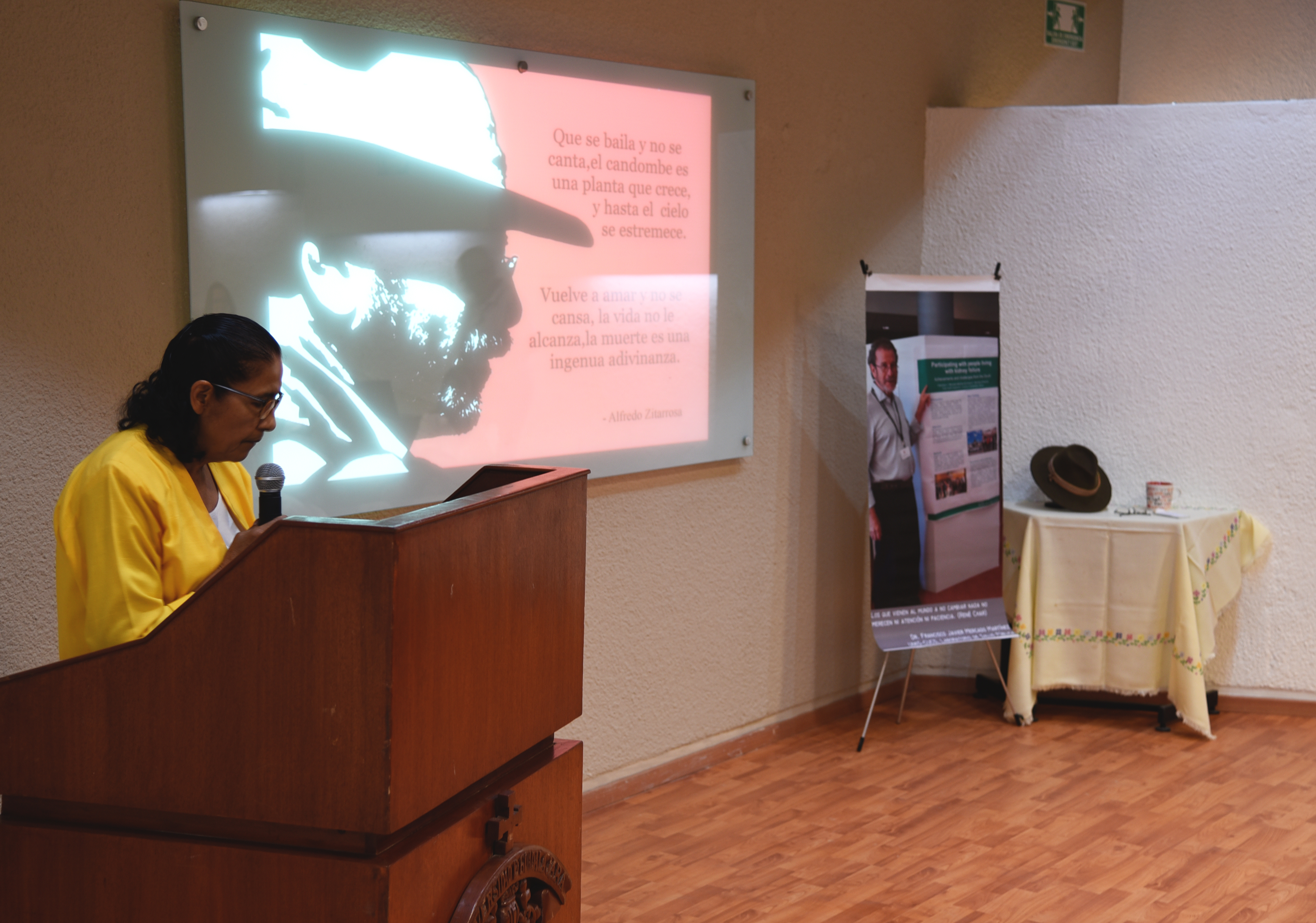 Dra. Amparo Tapia en pódium. Al fondo foto de perfil y pertenencias del Dr. Mercado