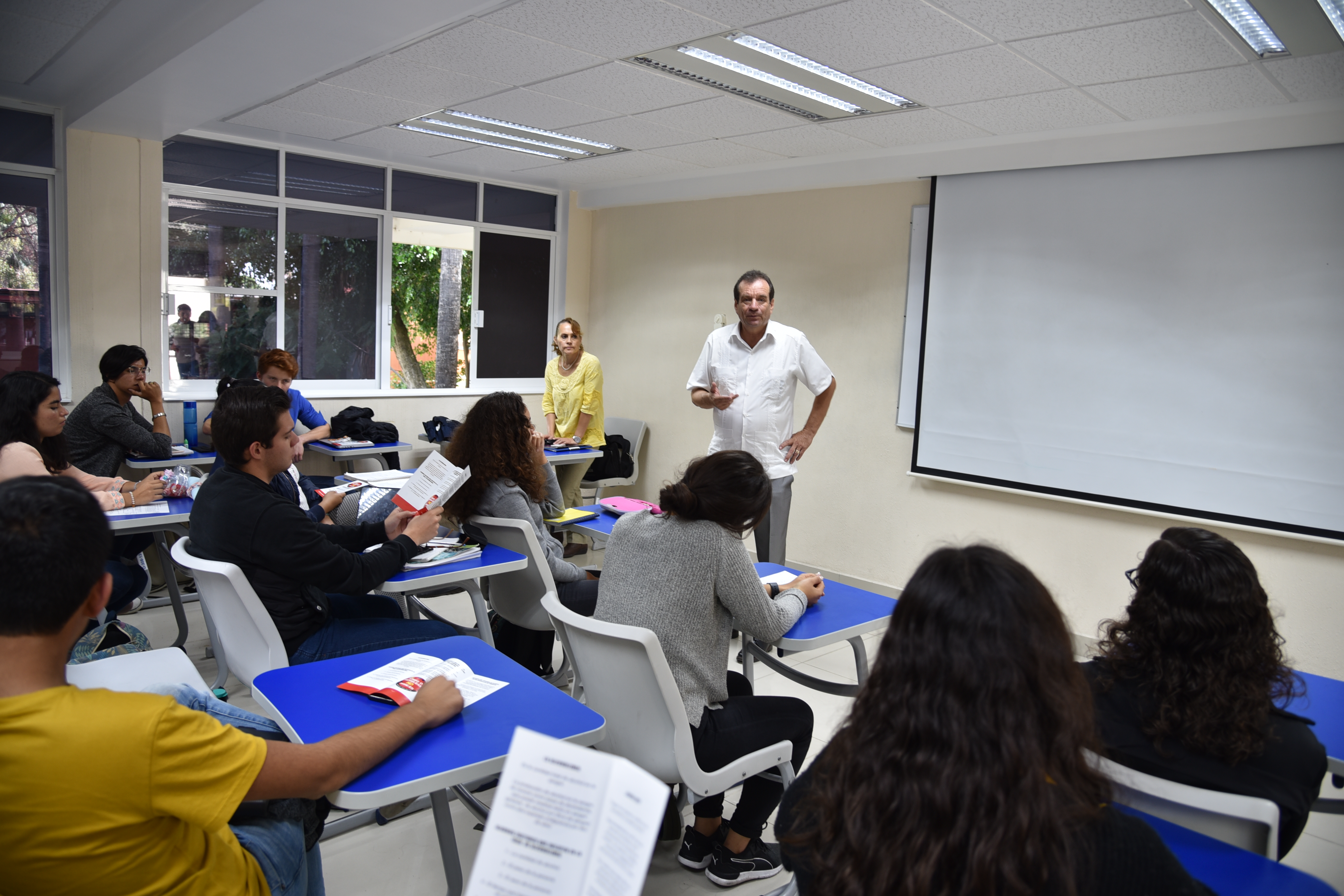 Diputado en salón de clases. Toma desde atrás del aula, alumnos con folletos abiertos