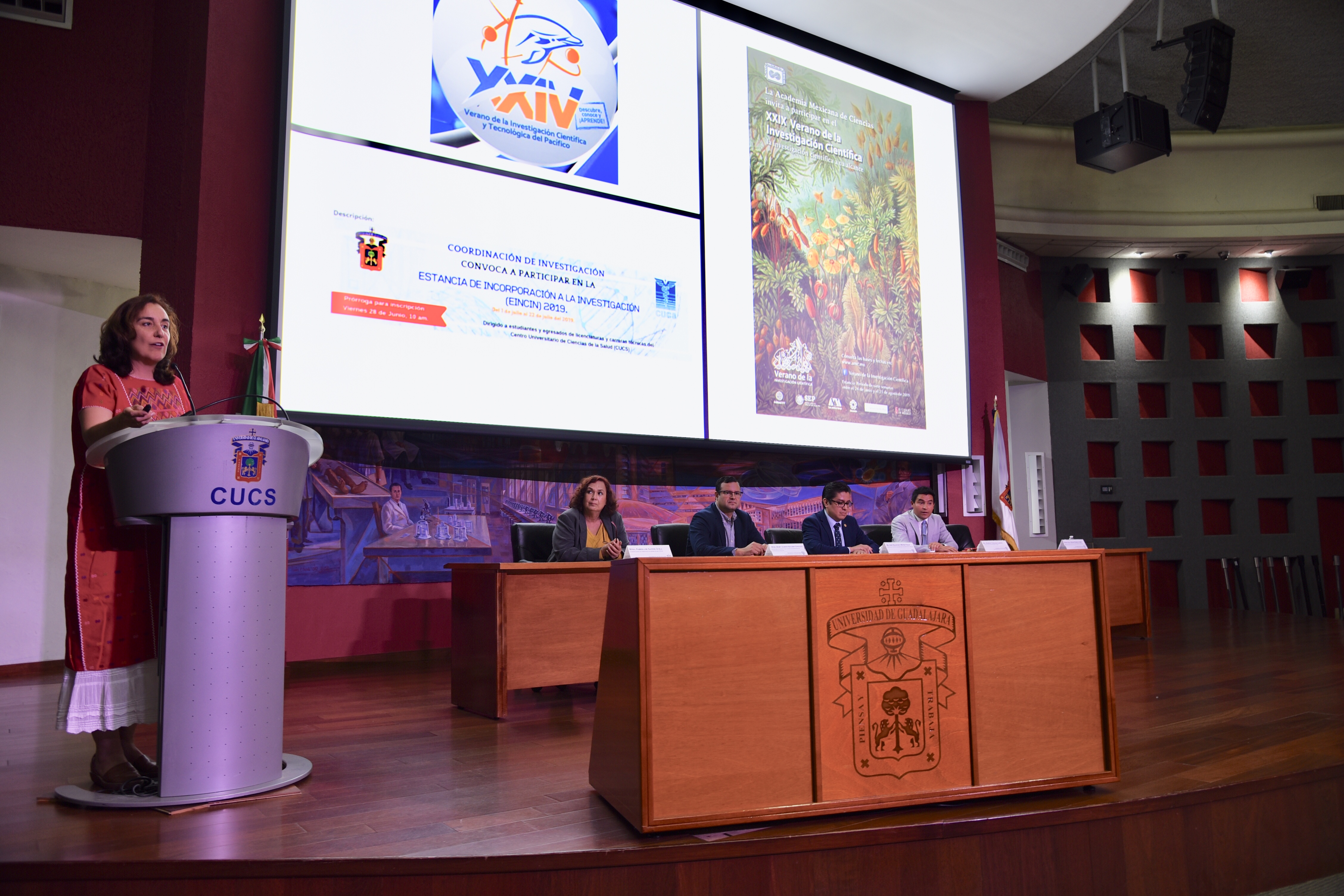 Miembros del presídium y al micrófono la coordinadora de Investigación