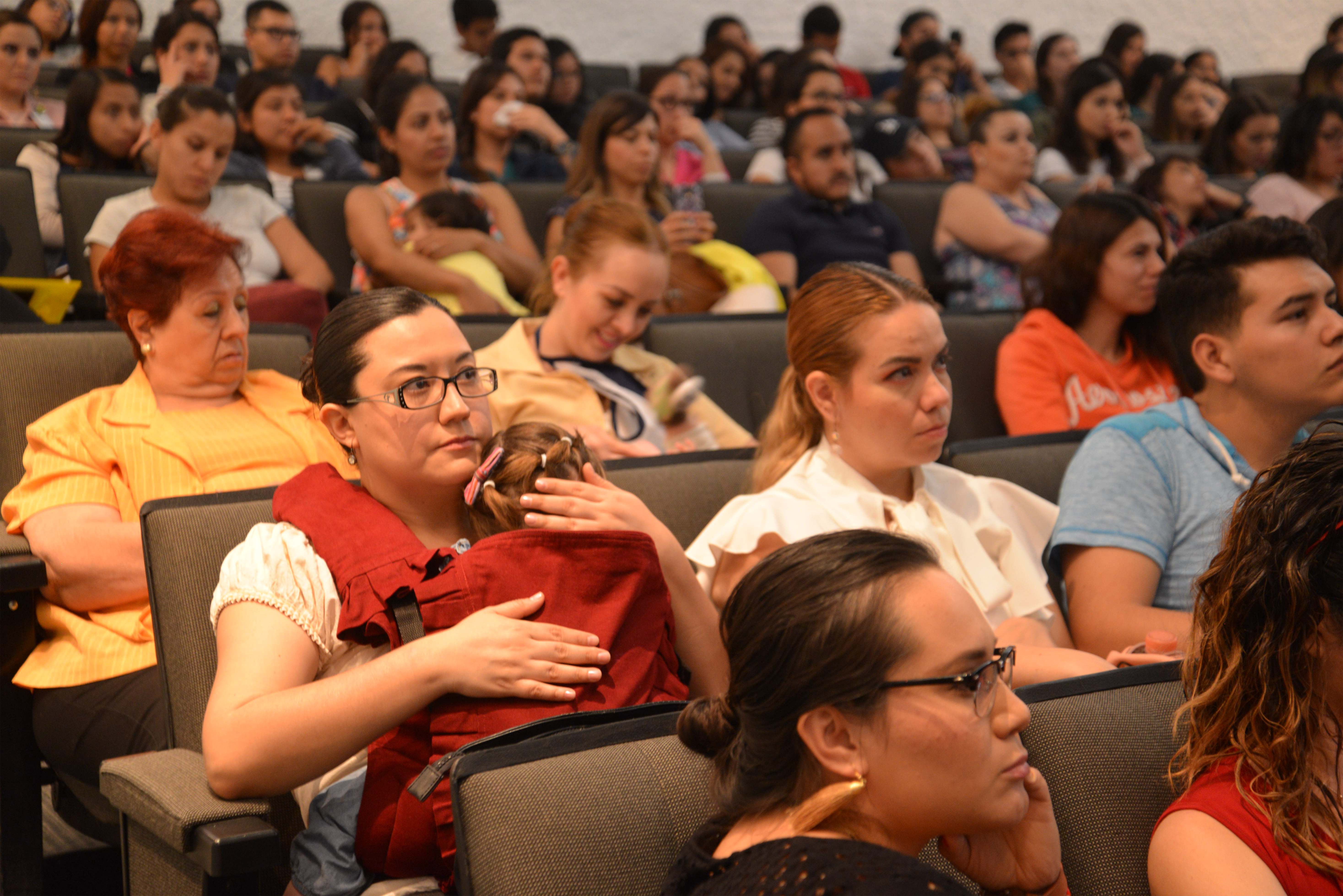 Mamá con su hija dormida en brazos escuchando la conferencia