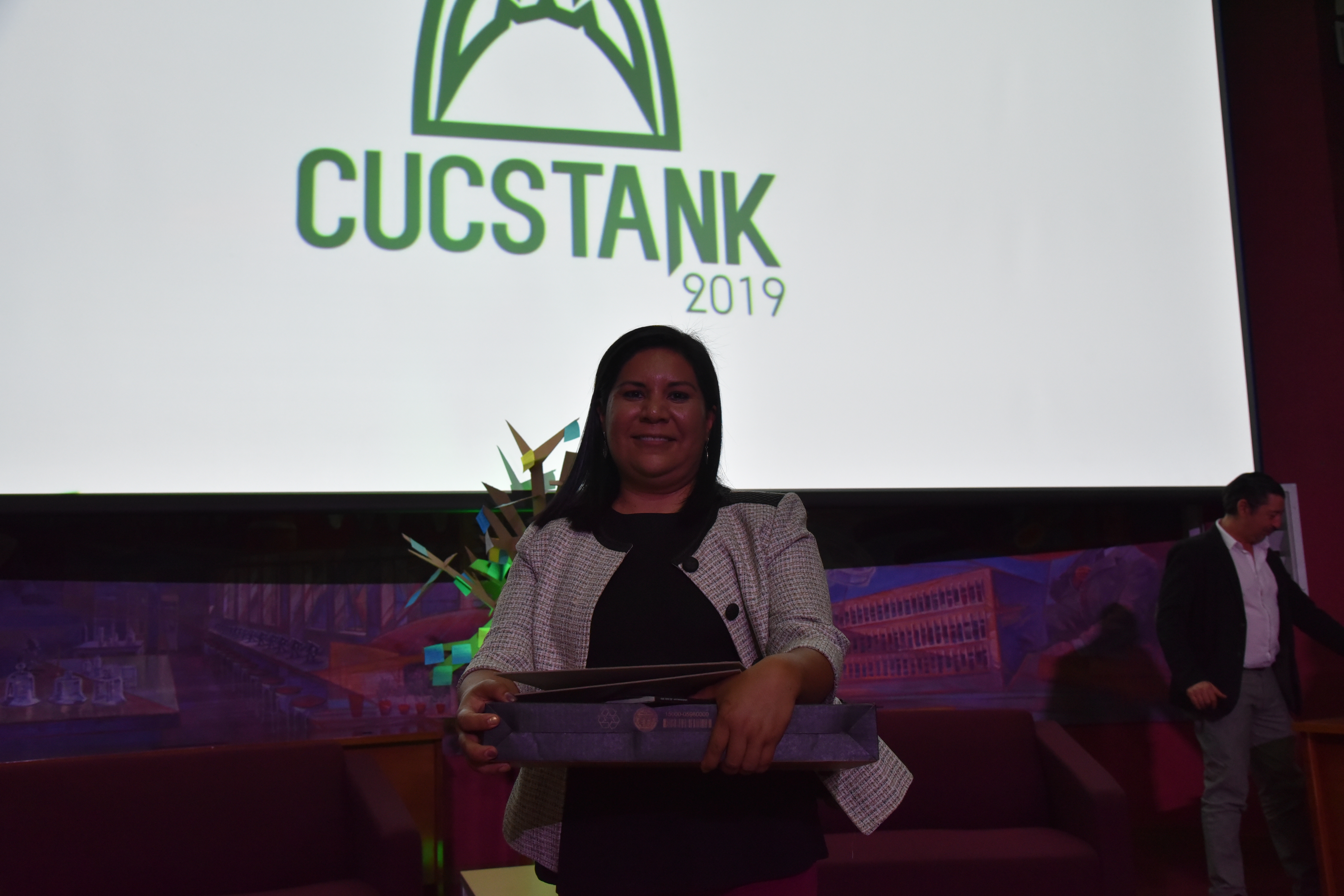 Dra. Sandra López Verdín exibiendo su  premio, al fondo pantalla con logotipo de CUCSTank