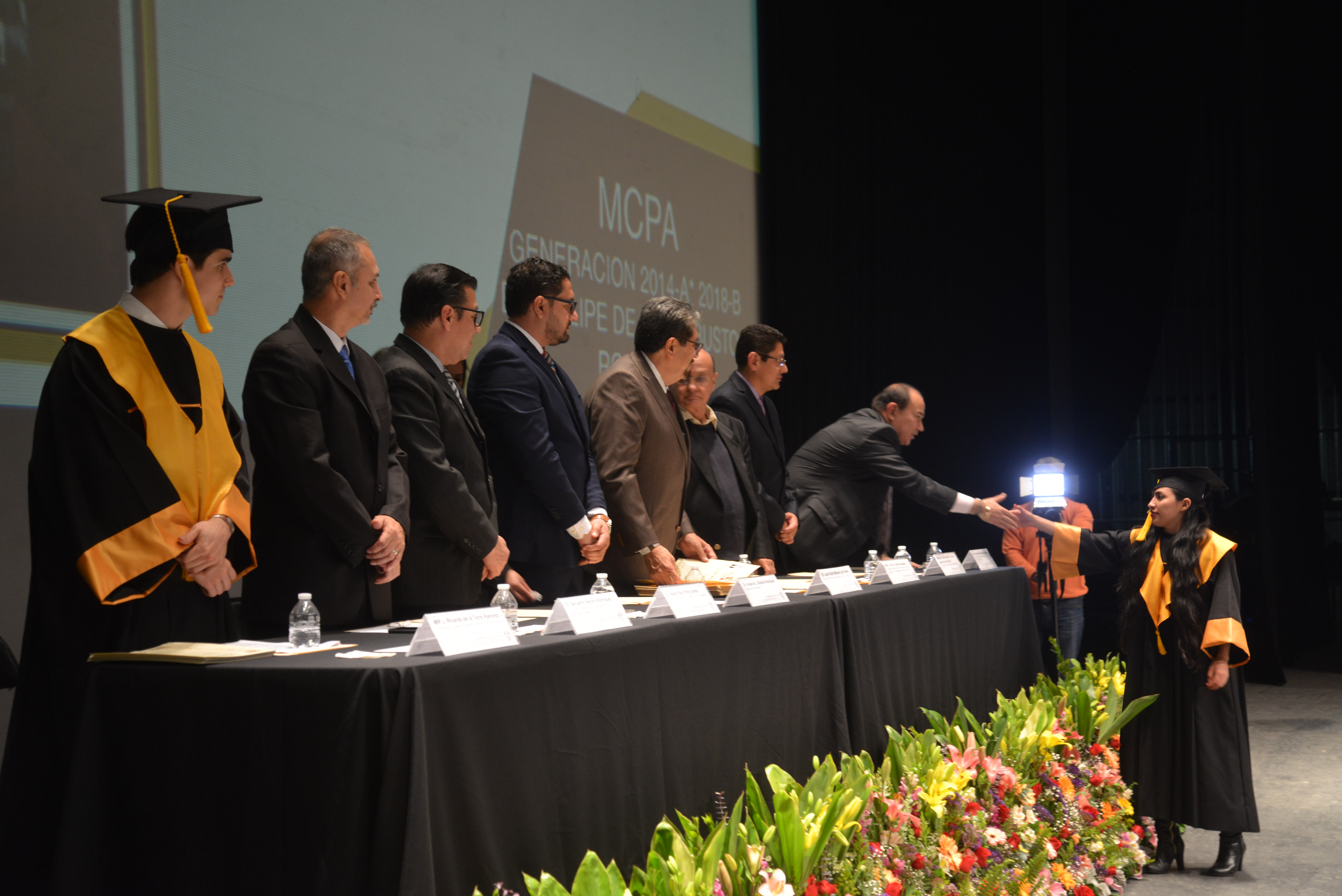 Graduado recibiendo su diploma y saludando a los miembros del presídium