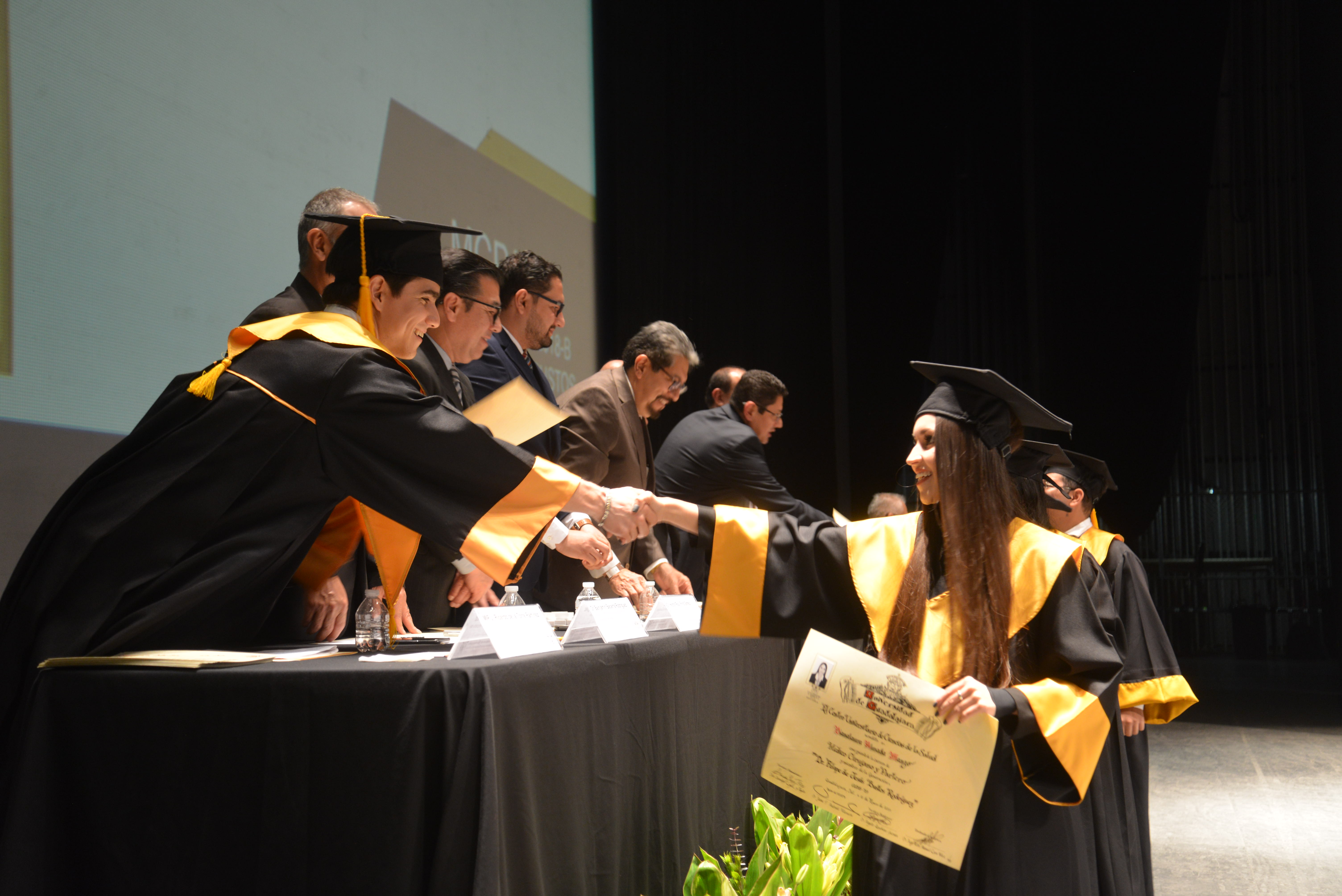 Graduada recibiendo su diploma y saludando a los miembros del presídium