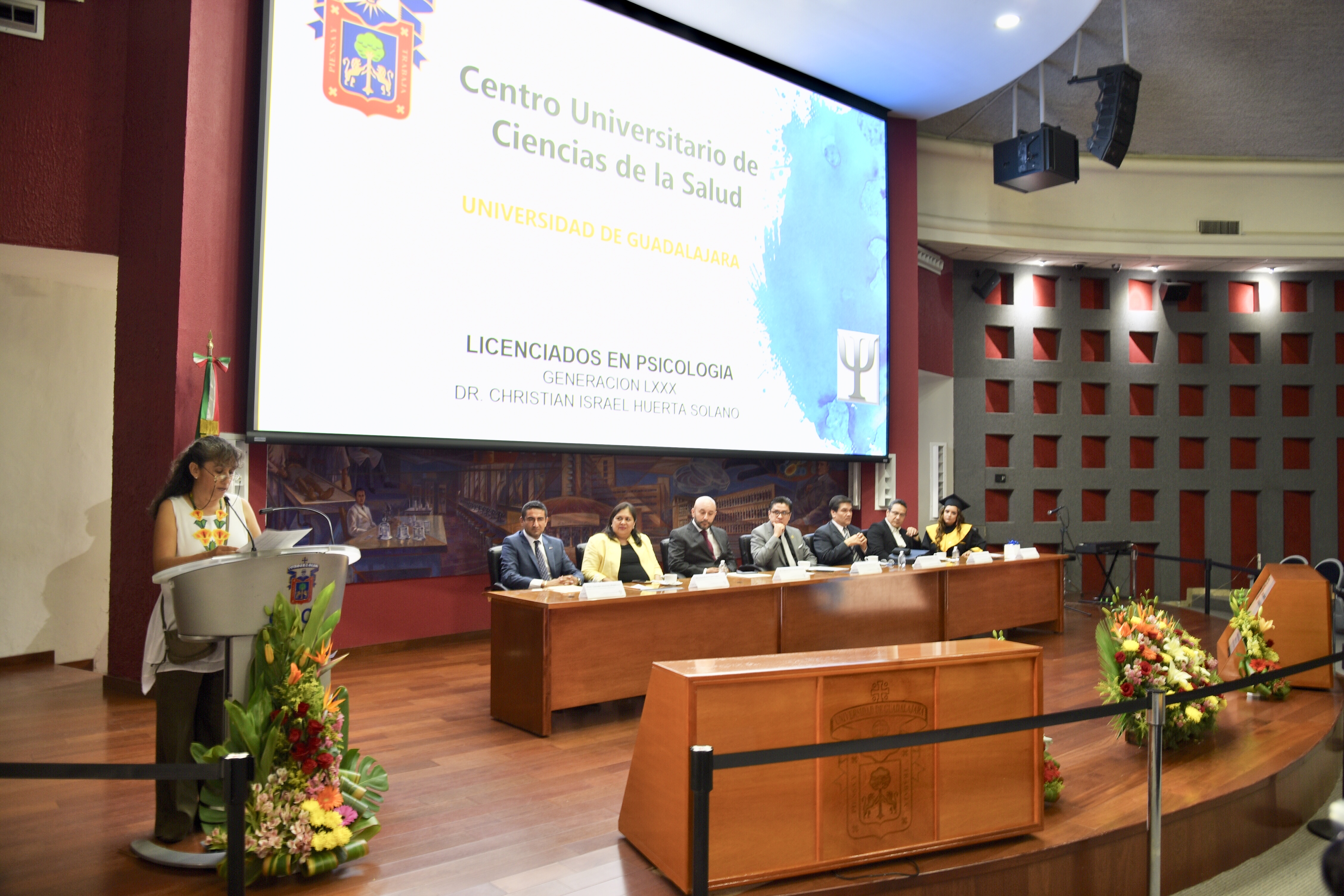 Miembros del presídium y al fondo en la pantalla imagen con el nombre del evento