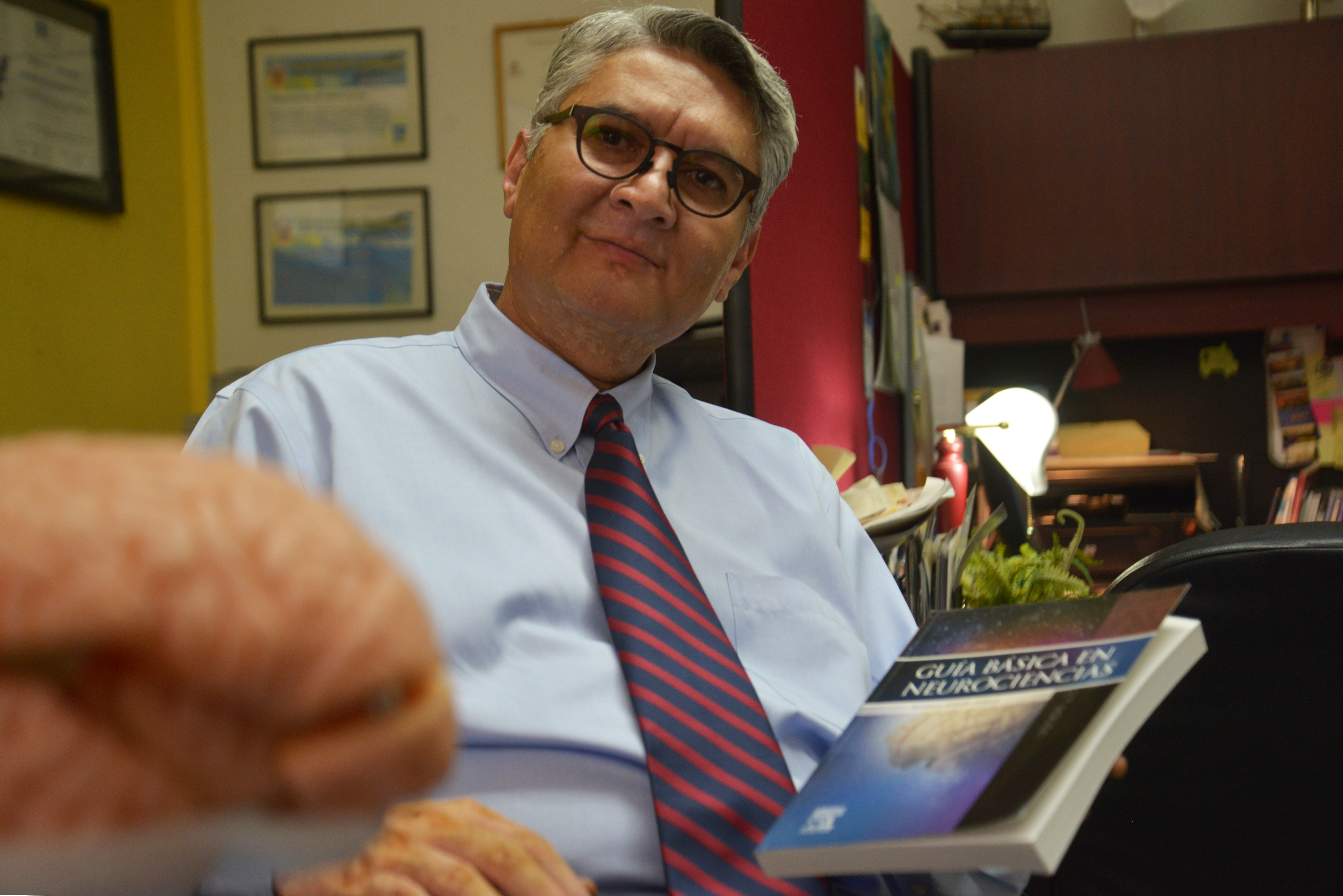 Dr. Rodrigo Ramos muestra el libro. En primer plano la réplica en silicón de un cerebro humano