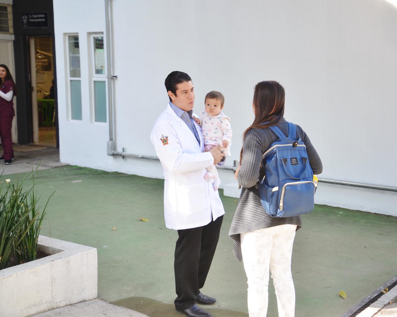 Coordinador Especialidad en Odontopediatría, cargando a una bebé y recibiendo a una mamá en la clínica