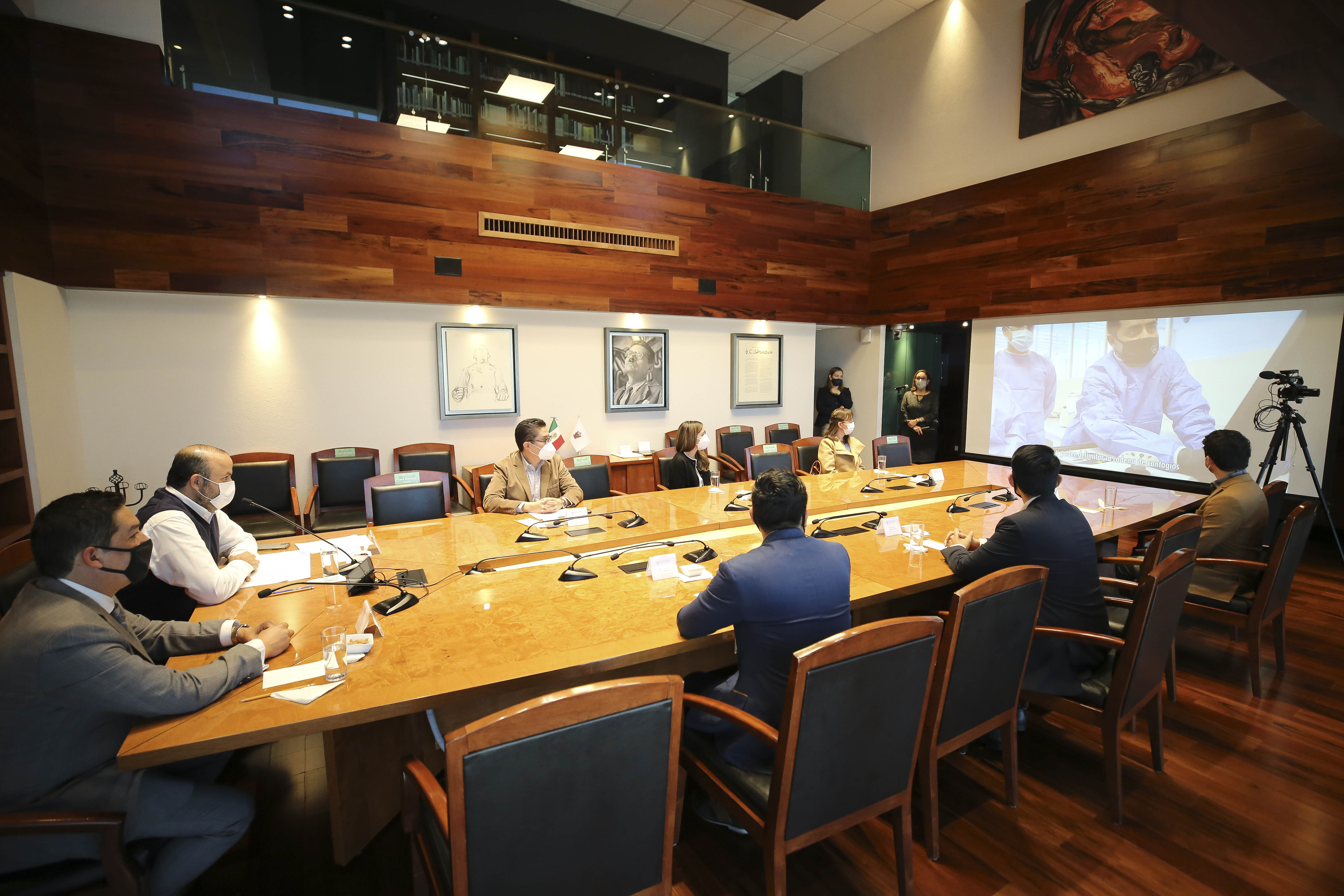 Funcionarios y directivos en sesión en la Sala Clemente Orozco, observan un video