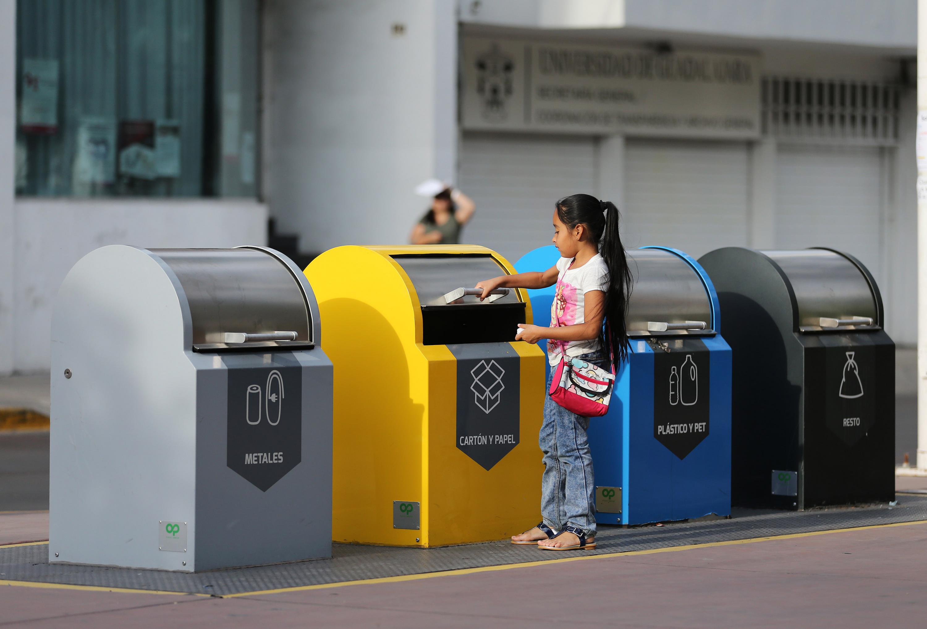 Contenedores de colores para seprar la basura, una niña depositando desechos en uno de ellos