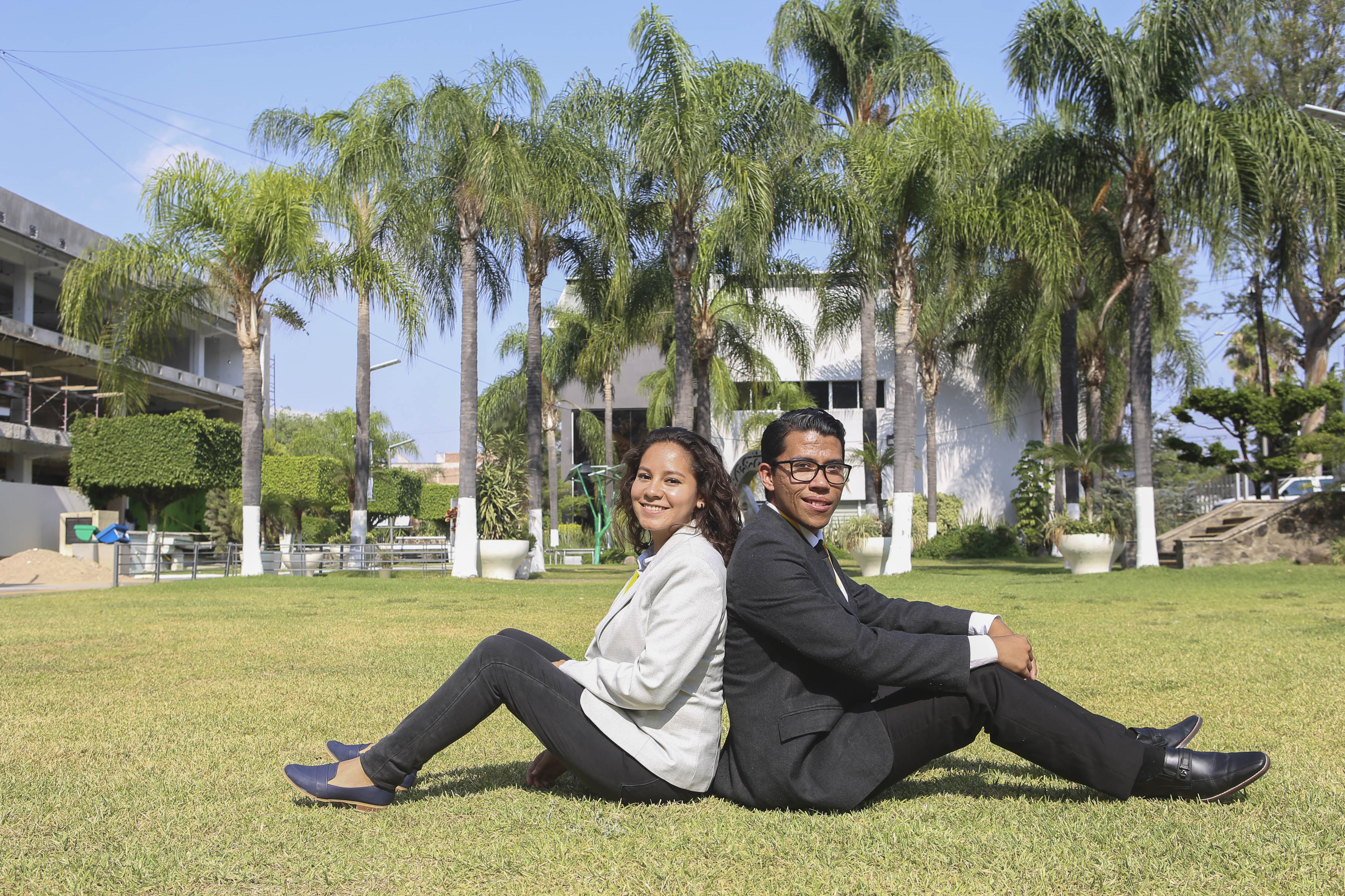 Alumnos sentados recargando sus espaldas entre sí, en jardines de Rectoría