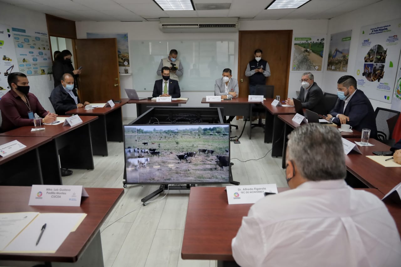 Toma desde atrás del salón de sesiones con funcionarios presentes y computadoras con la sesión virtual