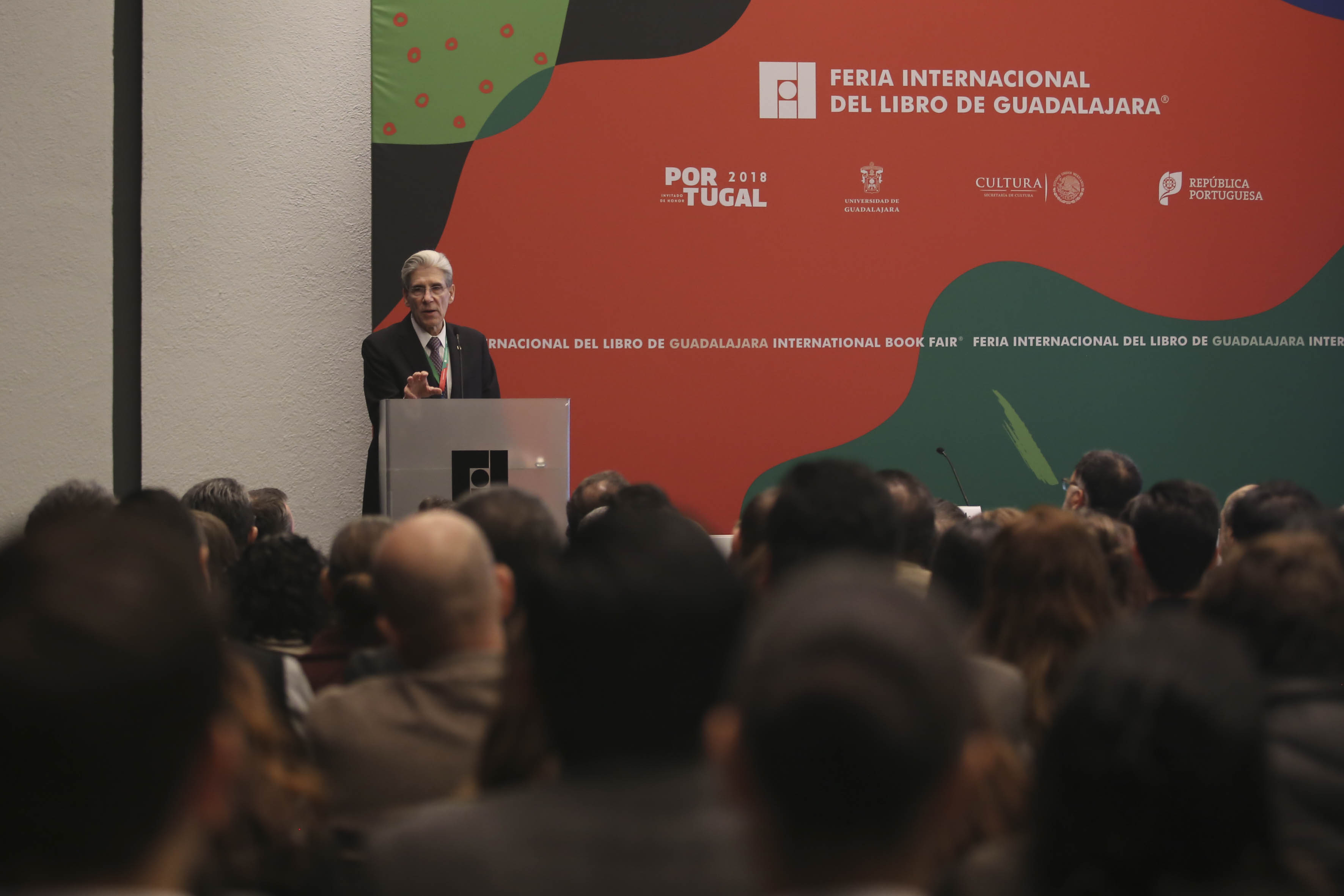 Dr. Julio Frenk al fondo del salón, antes se ven personas sentadas en un salón a lleno total