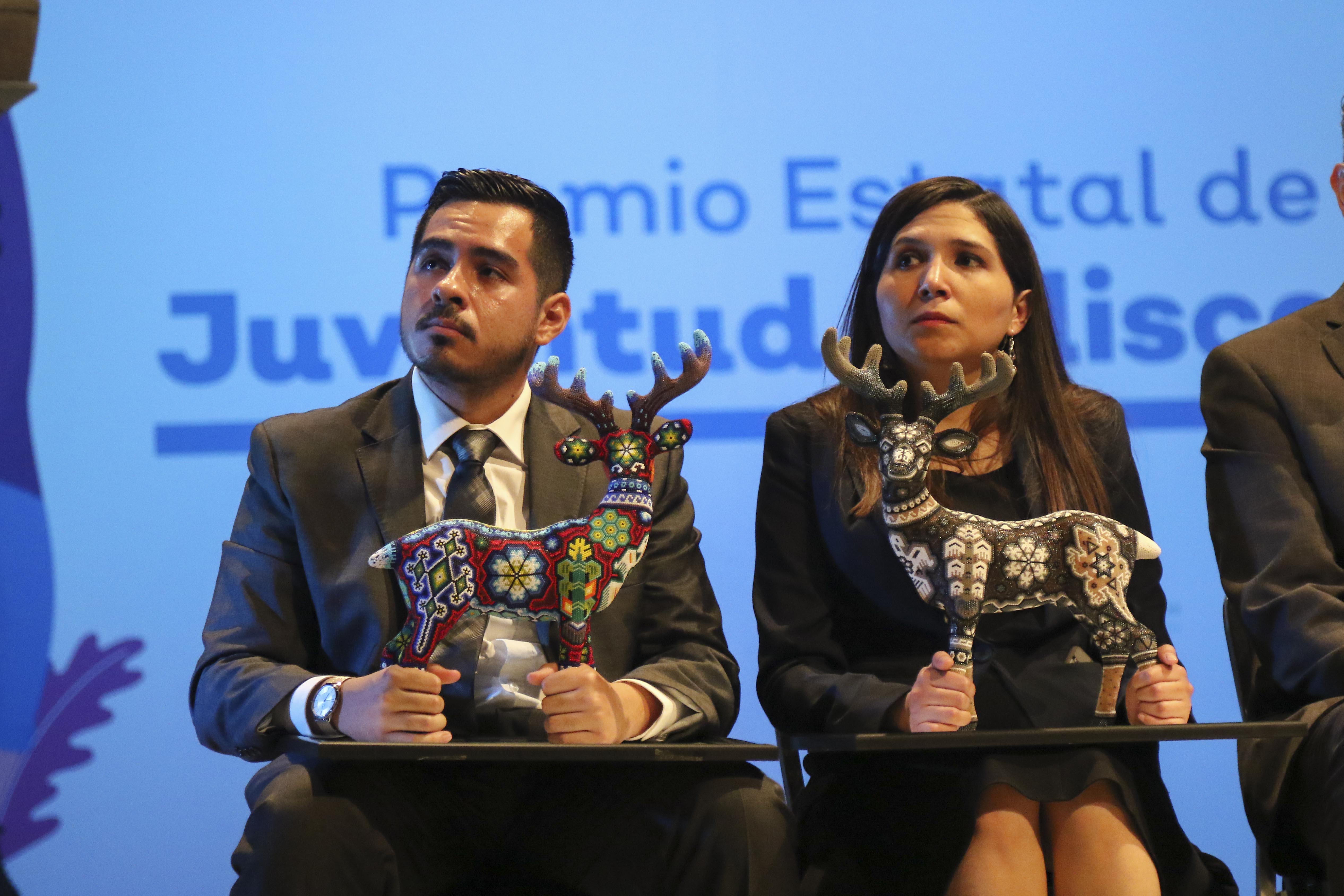 Egresados de UdeG escuchando al ponente, tienen en sus manos el galardón con el que los premiaron