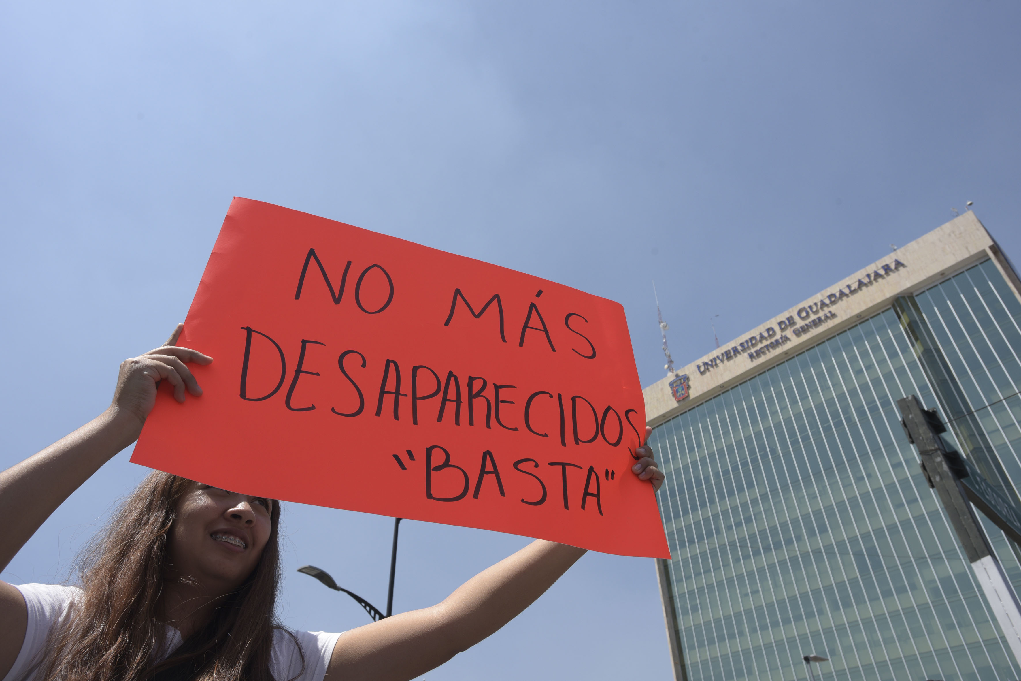 Estudiate exhibiendo letrero de protesta, al fondo edificio de Rectoría General