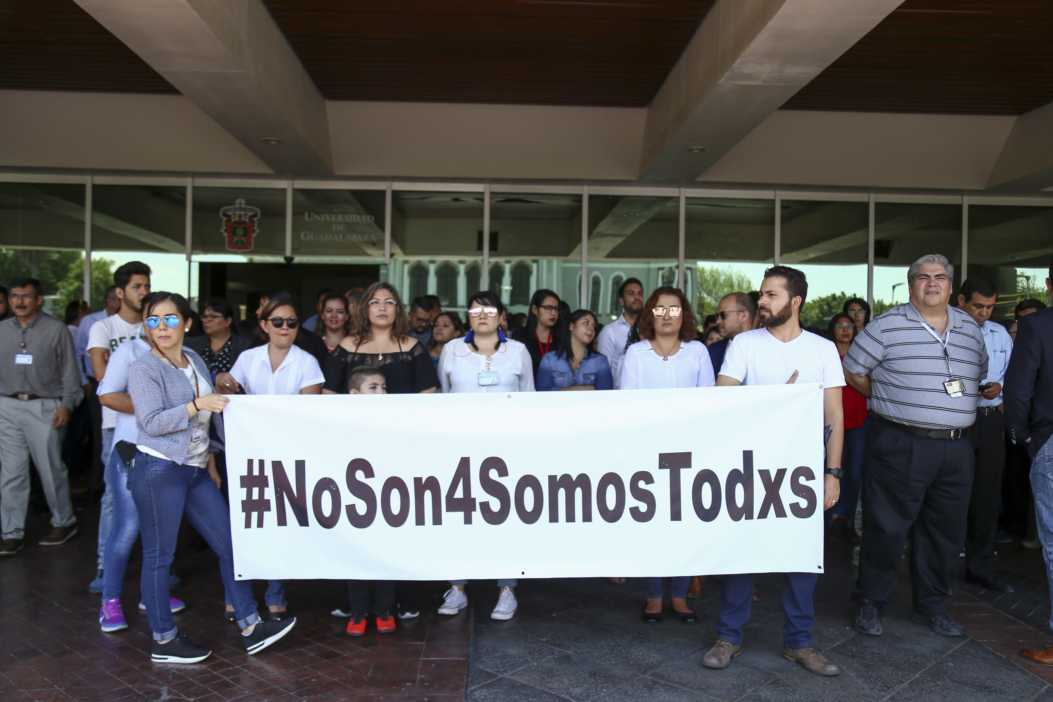 Foto a las puertas del edificio de Rectoría General con alumnos, trabajadores, docentes y funcionarios exhibiendo una manta de protesta