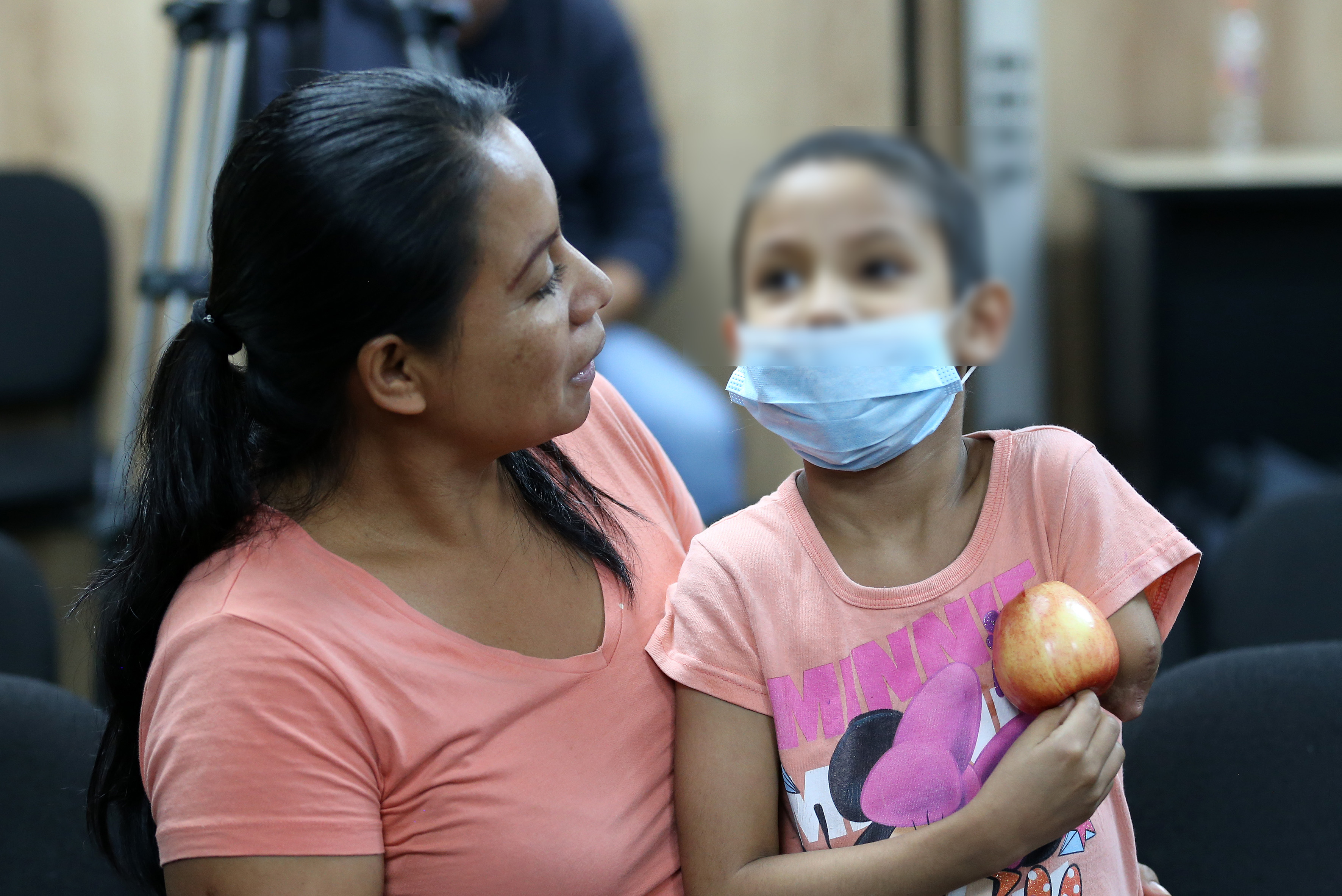 Mamá abrazando a su hija con cáncer, ella con cubrebocas