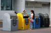 Contenedores de colores para seprar la basura, una niña depositando desechos en uno de ellos