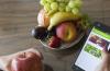 Frutas dispuestas en un plato al lado de un celular en la mano de una mujer en una página que dice menú