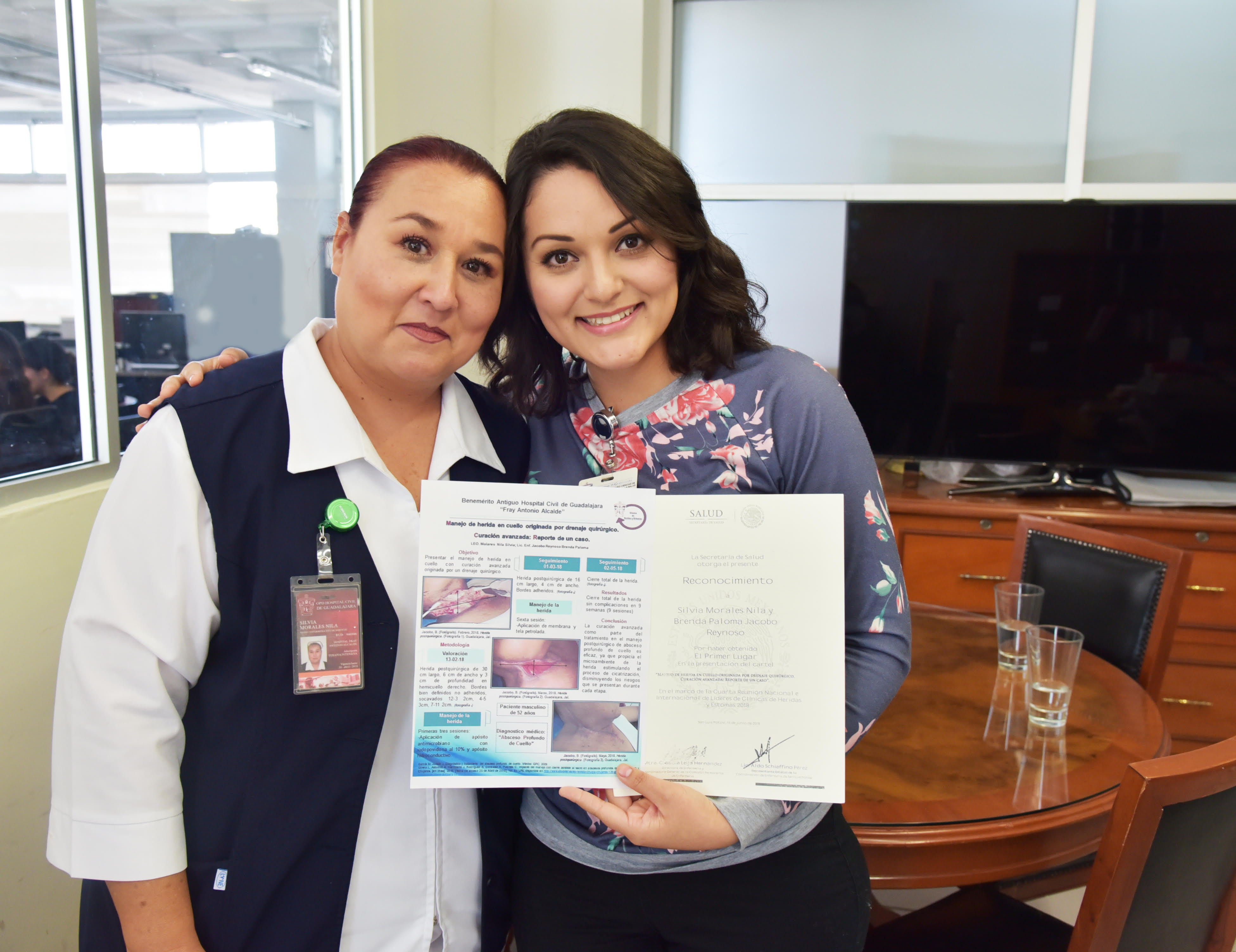 Alumna posando para la foto abrazando a su maestra y mostrando copia del cartel de investigación