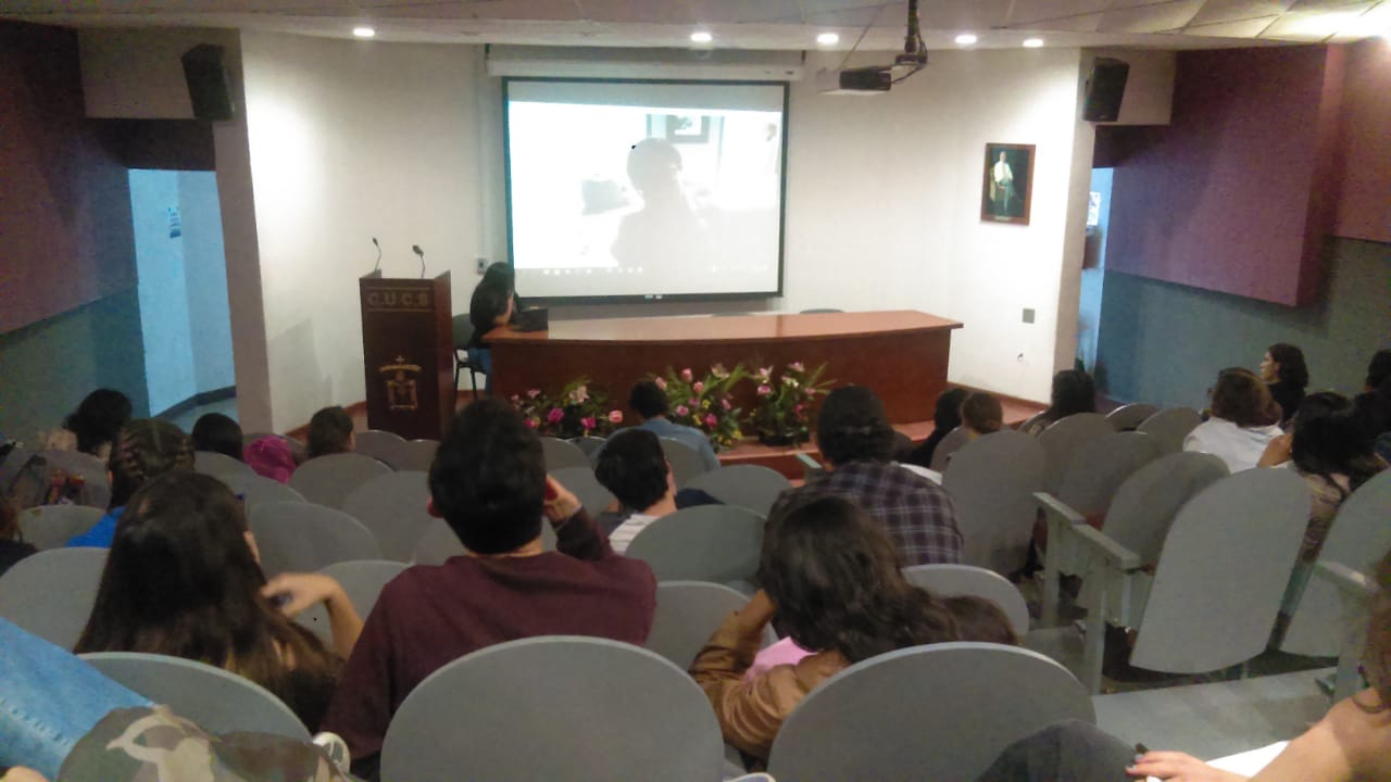 En la pantalla, la Dra. Gloria González. En el presídium, la Mtra. Verónica Rubí Beltrán transmitiendo la conferencia